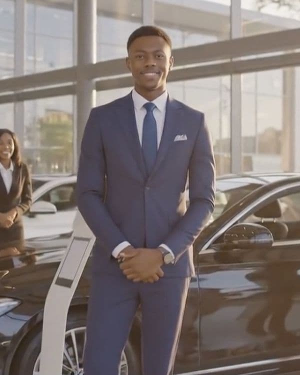 A young South African professional standing confidently in a car showroom — dealership-ready and prepared